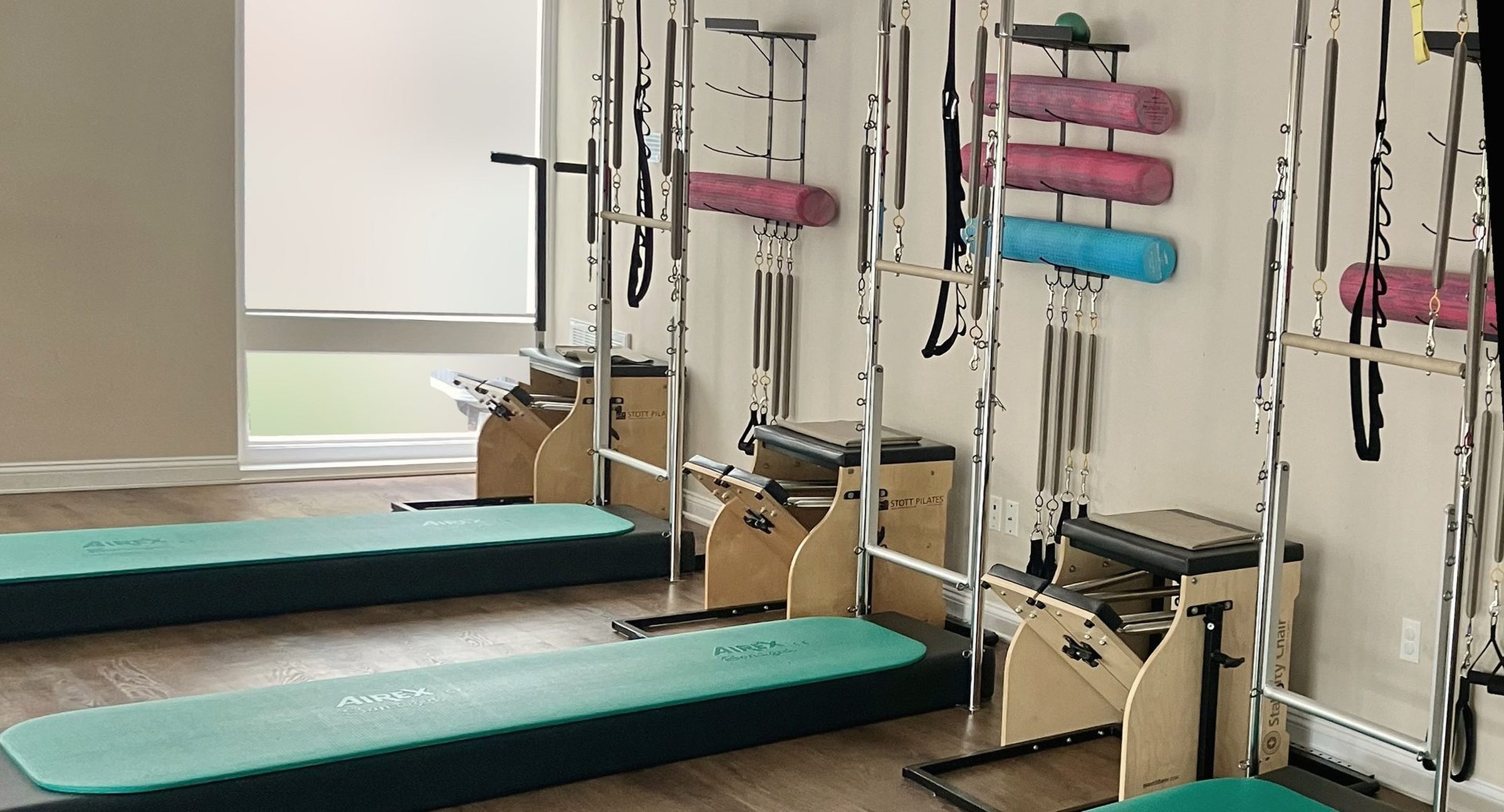 Tower stations, teal mats and wooden Pilates chairs along the studio wall.