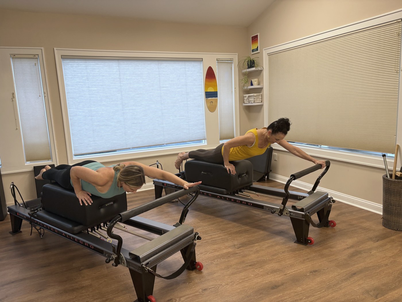 Nicole and a client lying on boxes on two reformers, side by side.