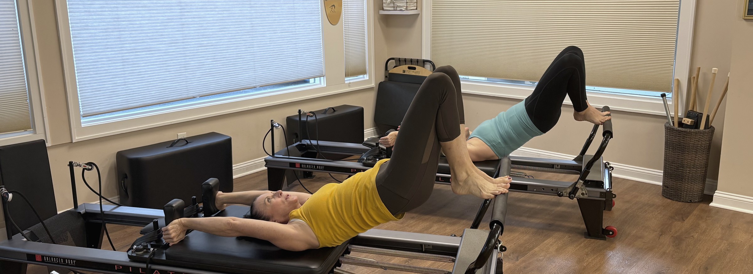 Nicole and a client practicing on reformers beside the studio windows.